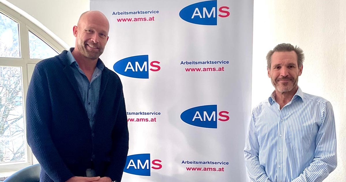 Nik Berger und Gottfried Lochner posieren vor einem AMS Banner zum gemeinsamen Foto