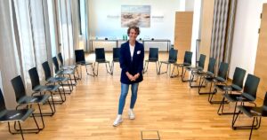 Gender Trainee Elena Breitenberger steht in der Mittel eines Sesselkreises in einem Seminarraum, kurz vor Beginn eines KADA Workshops