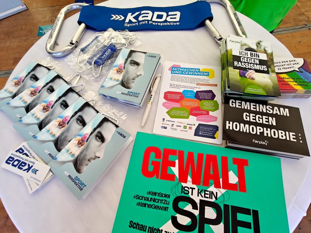 Auf einem Stehtisch liegen Infomaterialien von KADA und fairplay verteilt